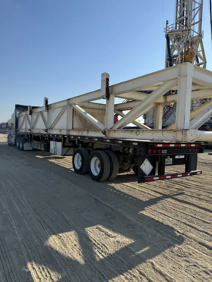 GTM Transport flatbed hauling a heavy steel truss beam at a drilling rig site
